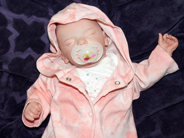 A baby doll peacefully sleeps on a soft white blanket, creating a serene and cozy scene.